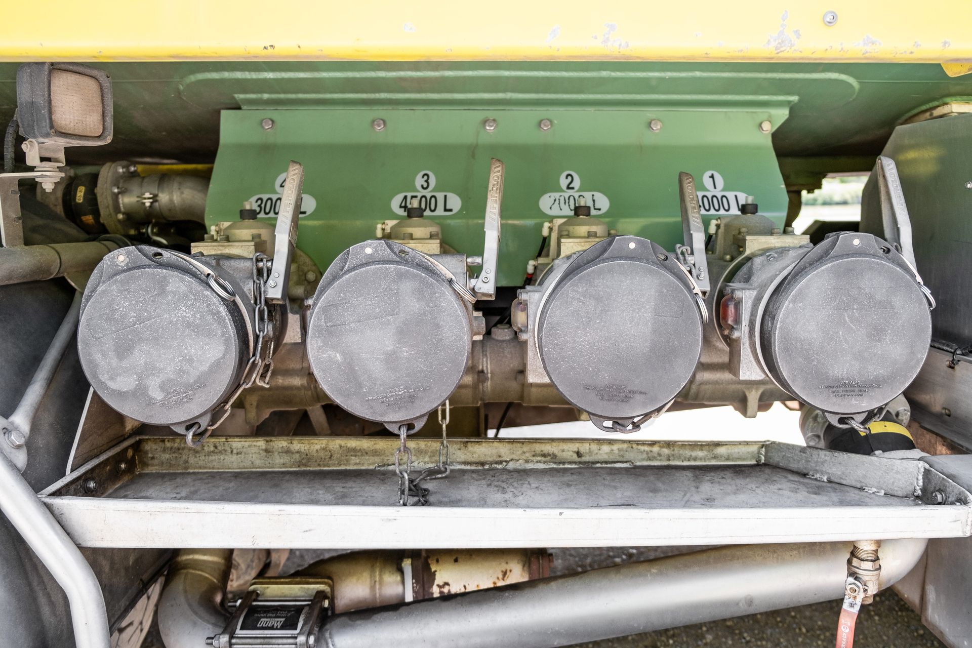 Quatre vannes de déchargement de carburant numérotées, munies de couvercles anti-poussière, sont placées au-dessus d'un bac de rétention des déversements sur un camion.