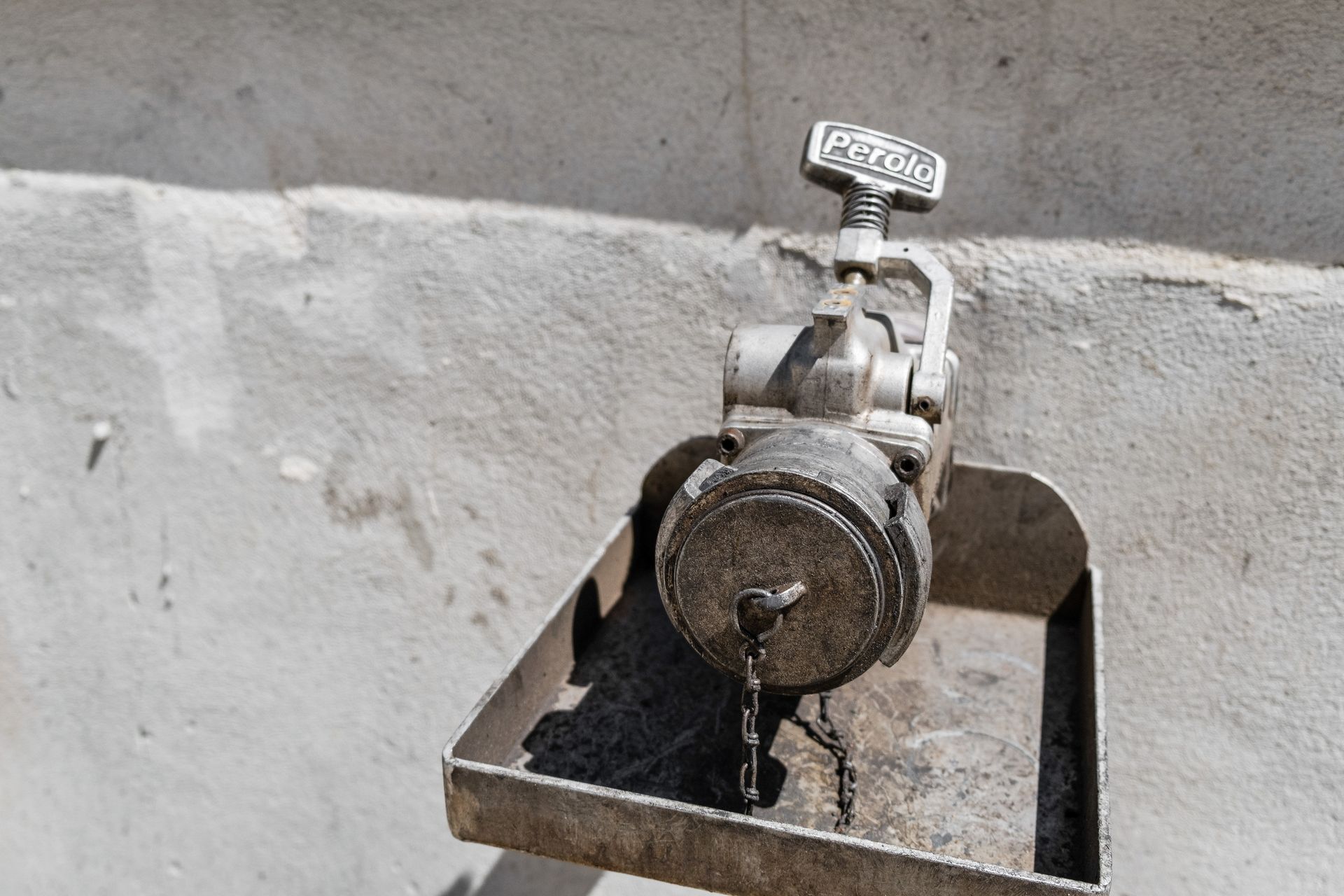 Gros plan sur un robinet en métal fixé sur un mur en béton brut, avec un petit bac de récupération sous le bec.