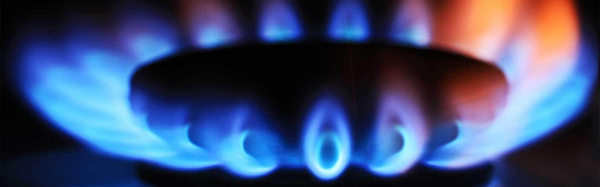 Gros plan sur un brûleur de cuisinière d'où émane un anneau de flammes bleu vif.