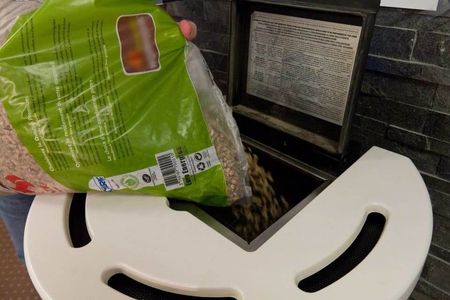 Une personne verse un sac de granulés de bois bruns dans la trémie ouverte d'un poêle à granulés.