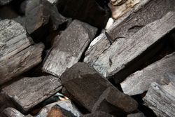 Gros plan sur un tas de morceaux de charbon de bois brut et foncé, aux textures variées et à la couleur gris-noir.