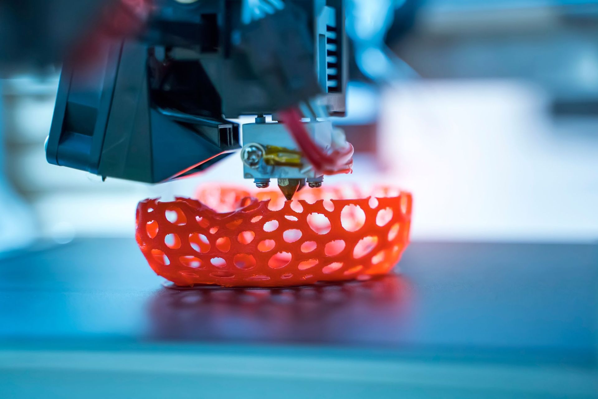 Una impresora 3D está imprimiendo un objeto rojo sobre una mesa.