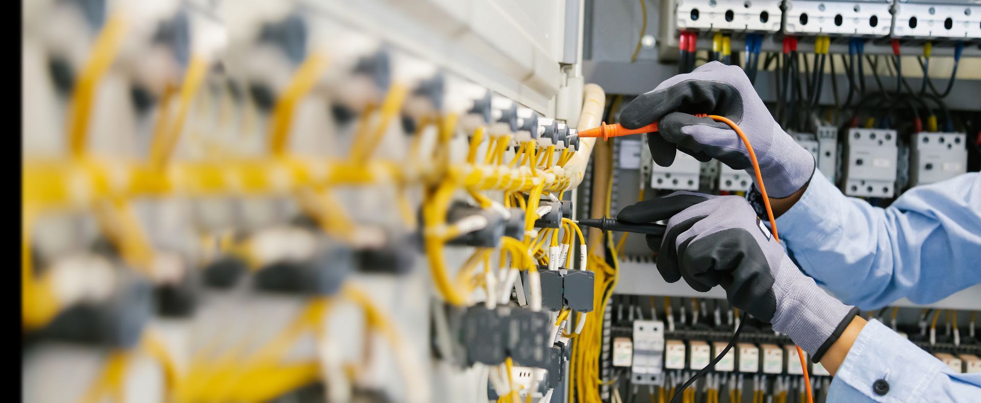 Un électricien portant des gants gris teste les fils d'un tableau électrique.