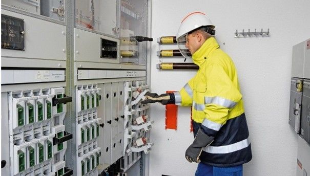 Un électricien portant des gants gris teste les fils d'un tableau électrique.