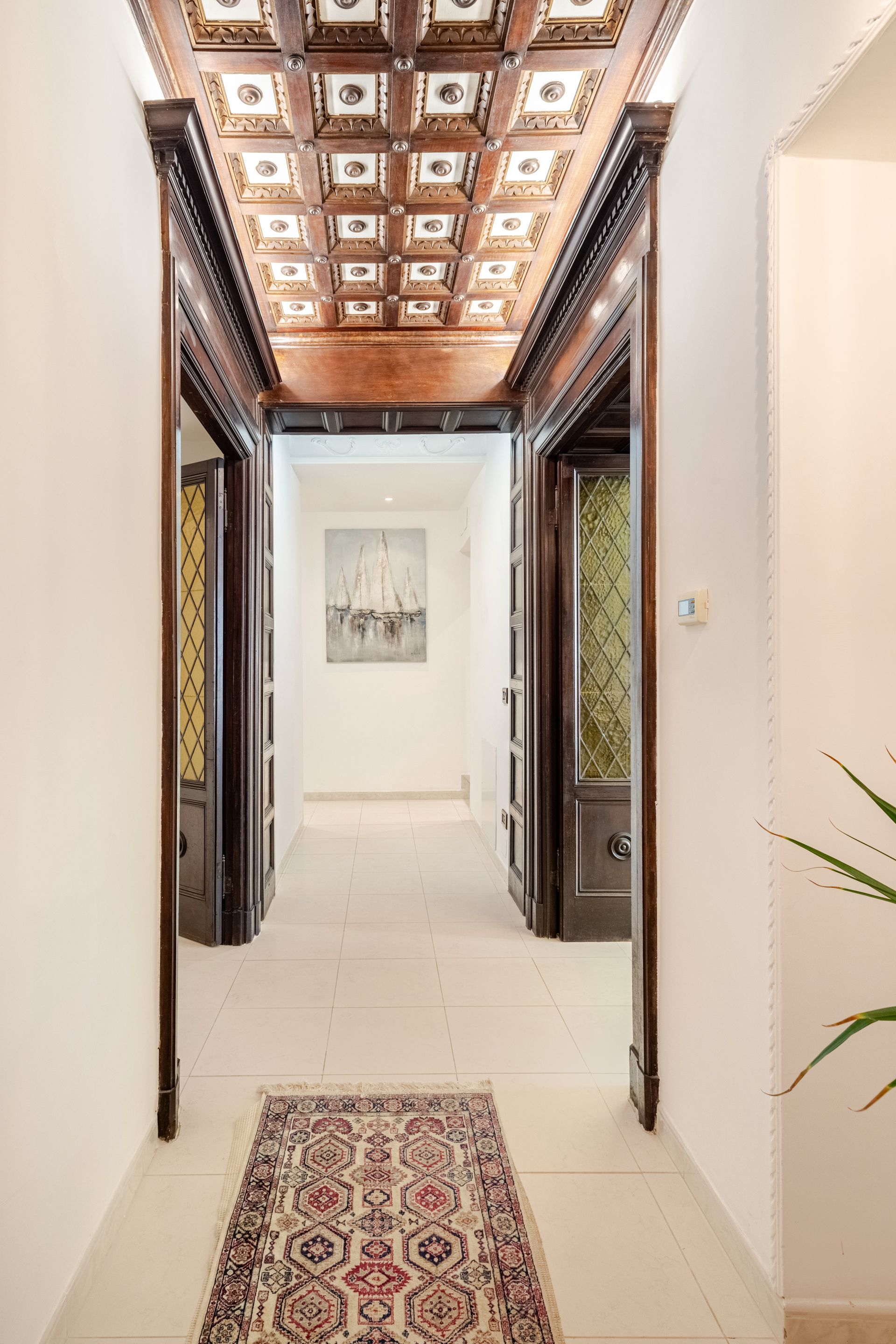 Long hallway with white walls, ornate wooden trim, and patterned rug; artwork at the end.