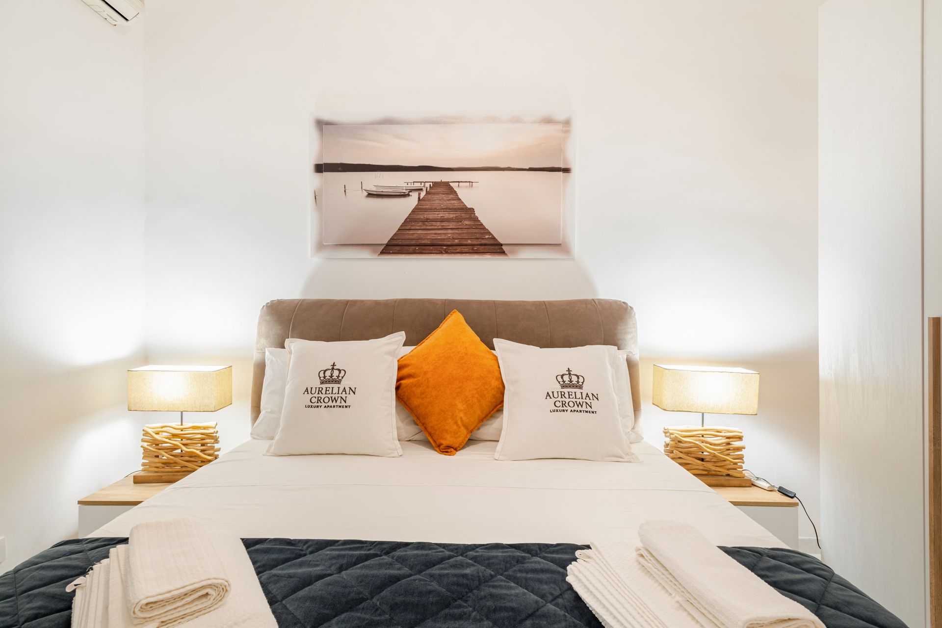 A bedroom with a double bed, featuring pillows, bedside lamps, and artwork above the headboard.