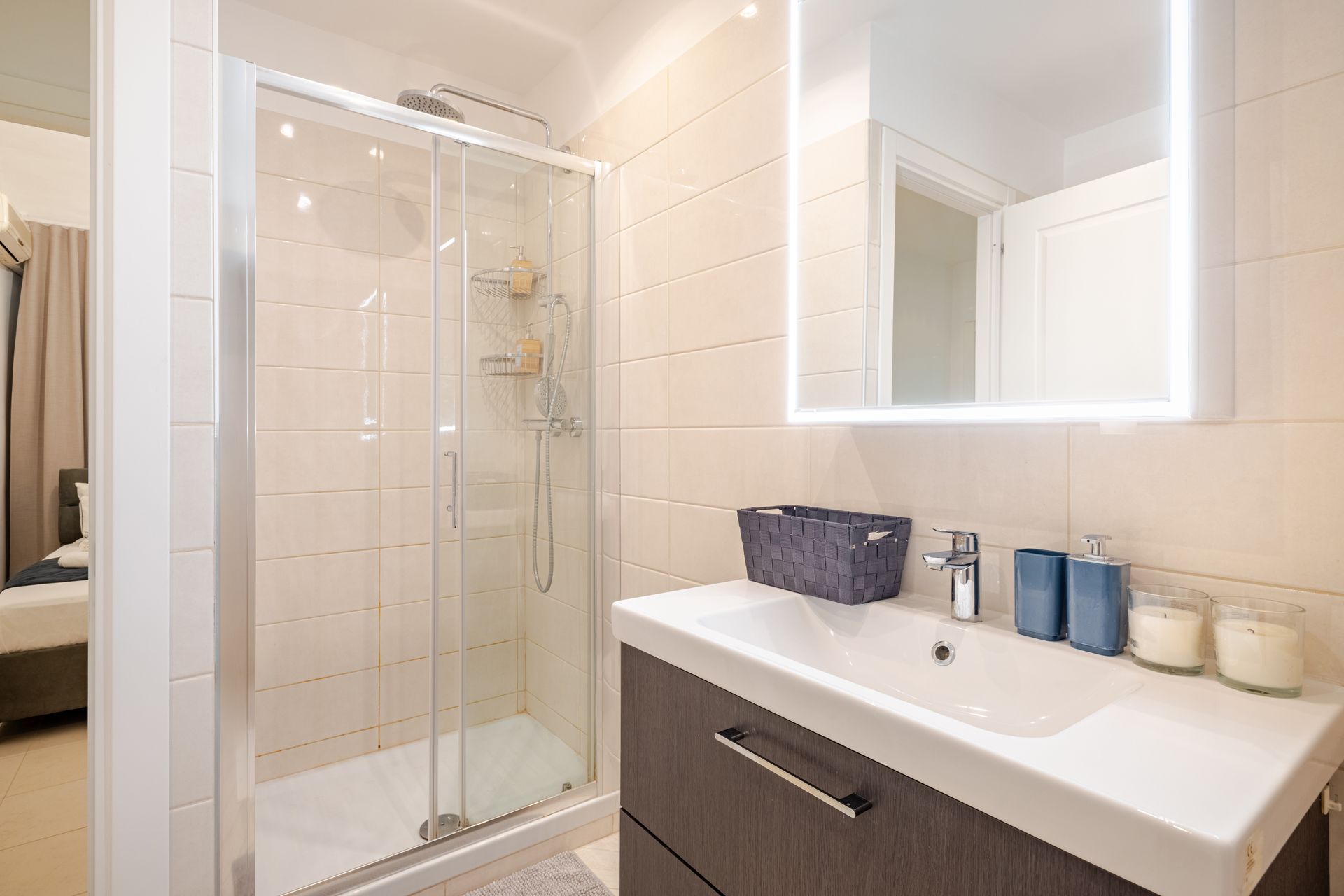 A modern bathroom featuring a glass shower, a white vanity with a dark brown cabinet, and a lit mirror.