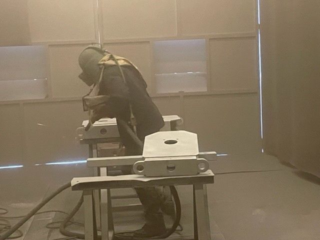 Homme en tenue spéciale réalisant un sablage de pièce dans l'atelier