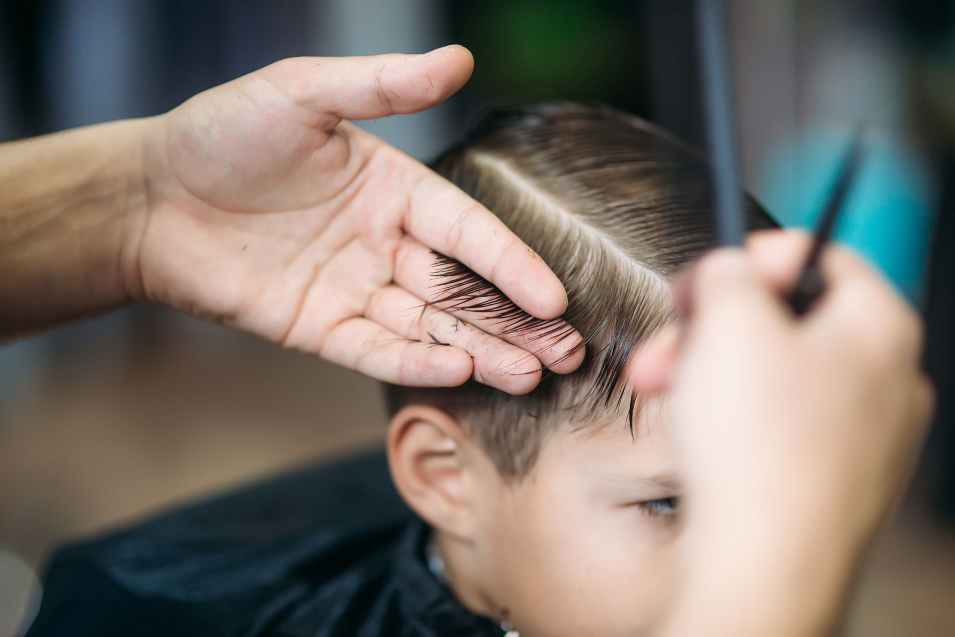 Ein kleiner Junge bekommt in einem Friseursalon einen Haarschnitt. Der Friseur kämmt ihm die Haare und trägt einen Seitenscheitel.