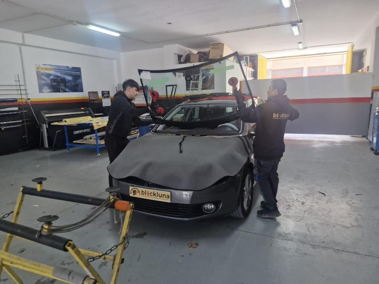 Dos trabajadores reemplazan el parabrisas de un automóvil en un taller de reparación; sosteniendo el vidrio.