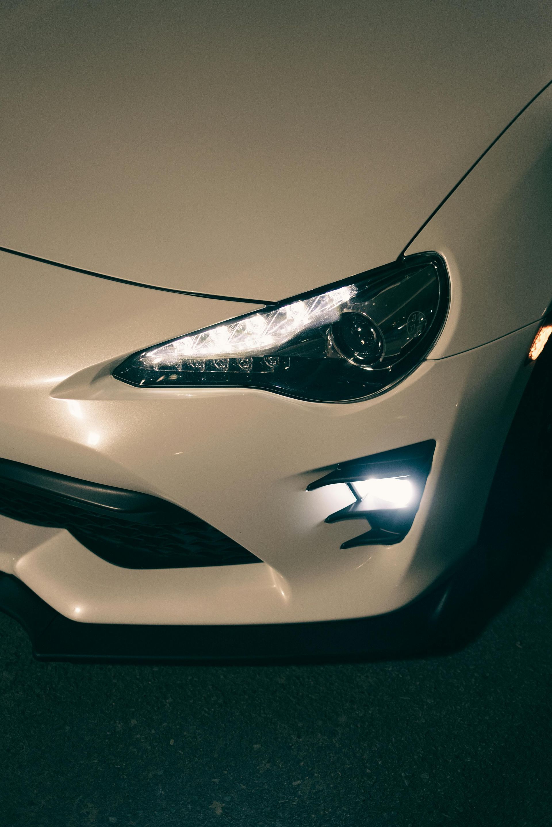 Parte delantera de un coche deportivo de color blanco, con faros encendidos, de noche.