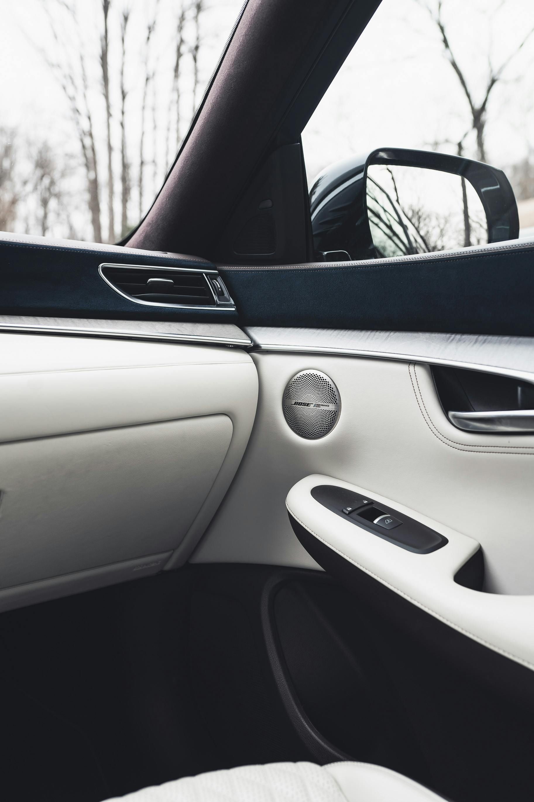 Detalle del interior del coche: panel de puerta de cuero blanco con altavoz, controles de ventana y espejo.