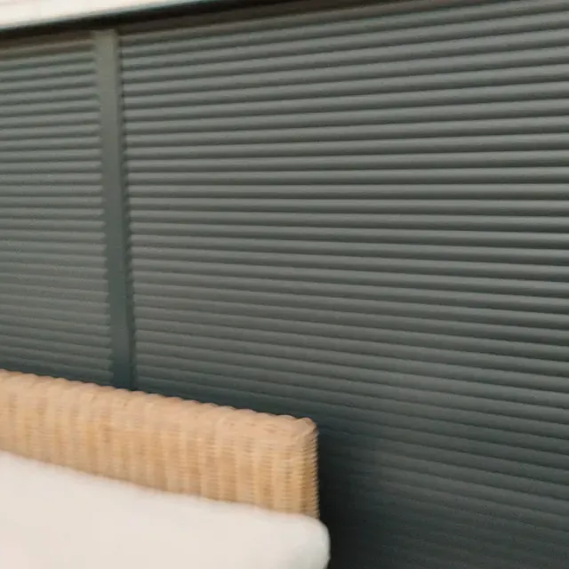 Una silla de mimbre está situada delante de una ventana con persianas.