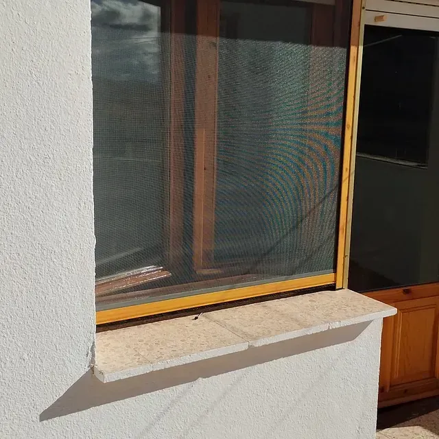 Una ventana con una mosquitera está en una pared blanca.