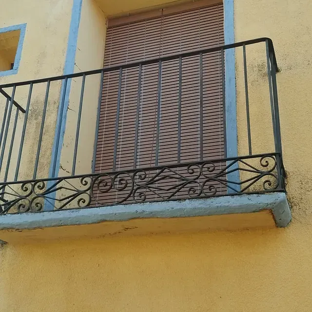 Un edificio amarillo con un balcón con barandilla de hierro forjado.