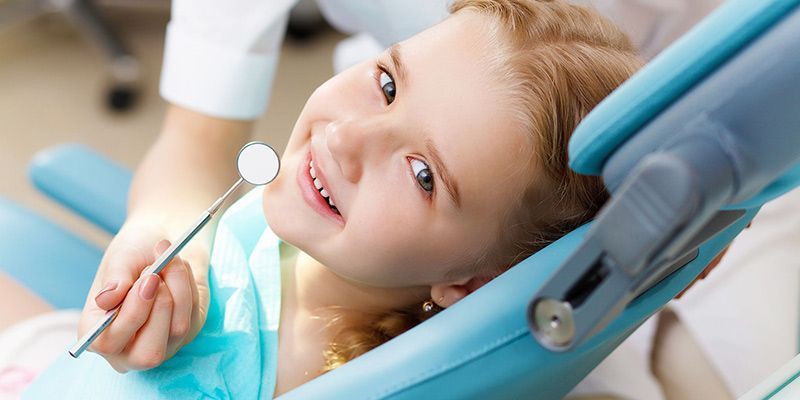 Una niña está sentada en una silla dental sosteniendo un espejo.