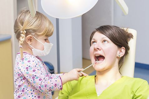 Una niña examina los dientes de una mujer en una silla dental.