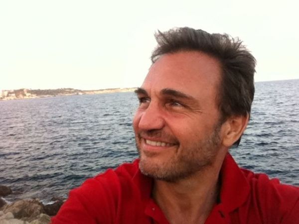 Un hombre con una camisa roja sonríe frente al océano.