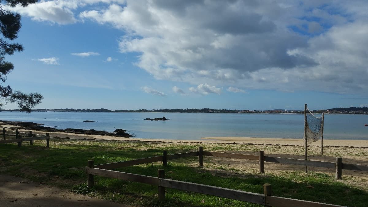Una valla de madera rodea una playa de arena con un cuerpo de agua al fondo.