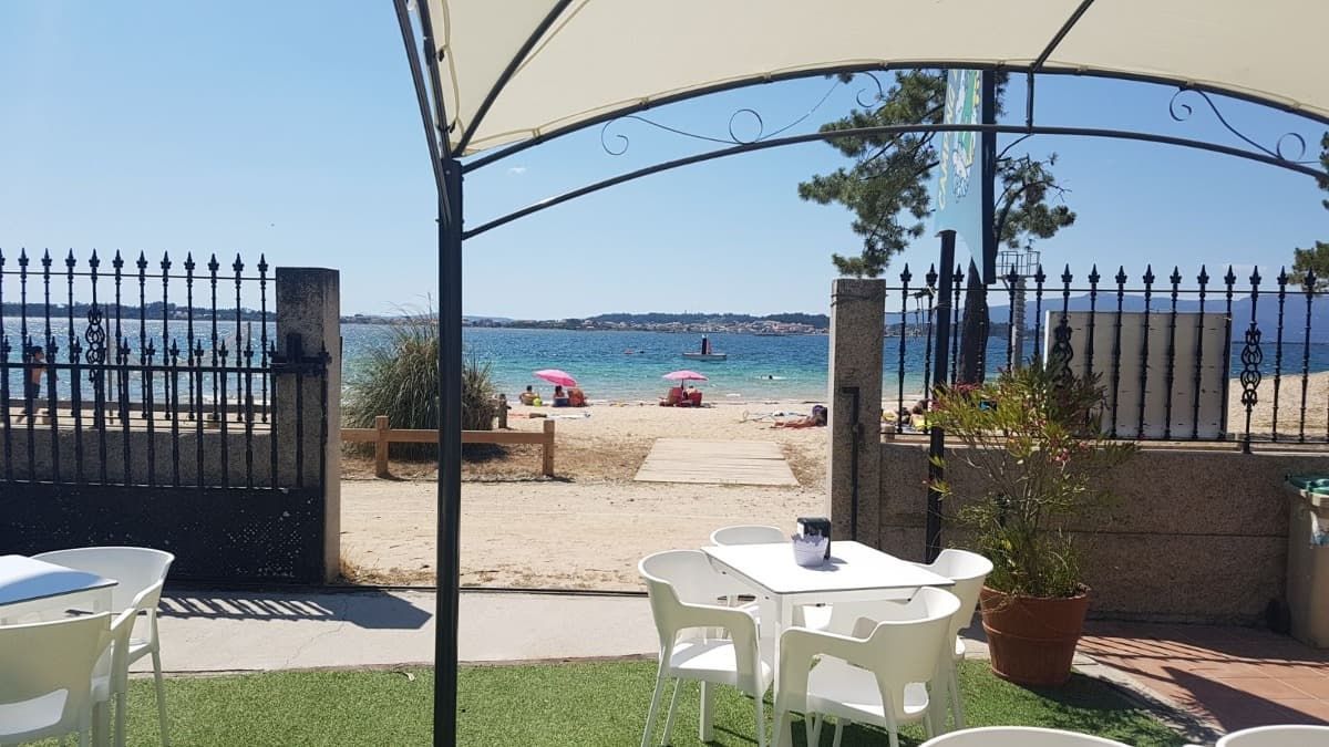Una vista de una playa desde un restaurante con mesas y sillas bajo una sombrilla.