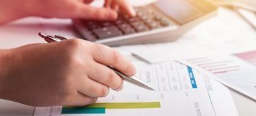 Manos usando un bolígrafo sobre gráficos y papeles impresos en un escritorio.