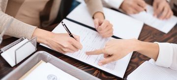 Manos tomando notas en una reunión de negocios alrededor de una mesa con papeles y cuadernos.