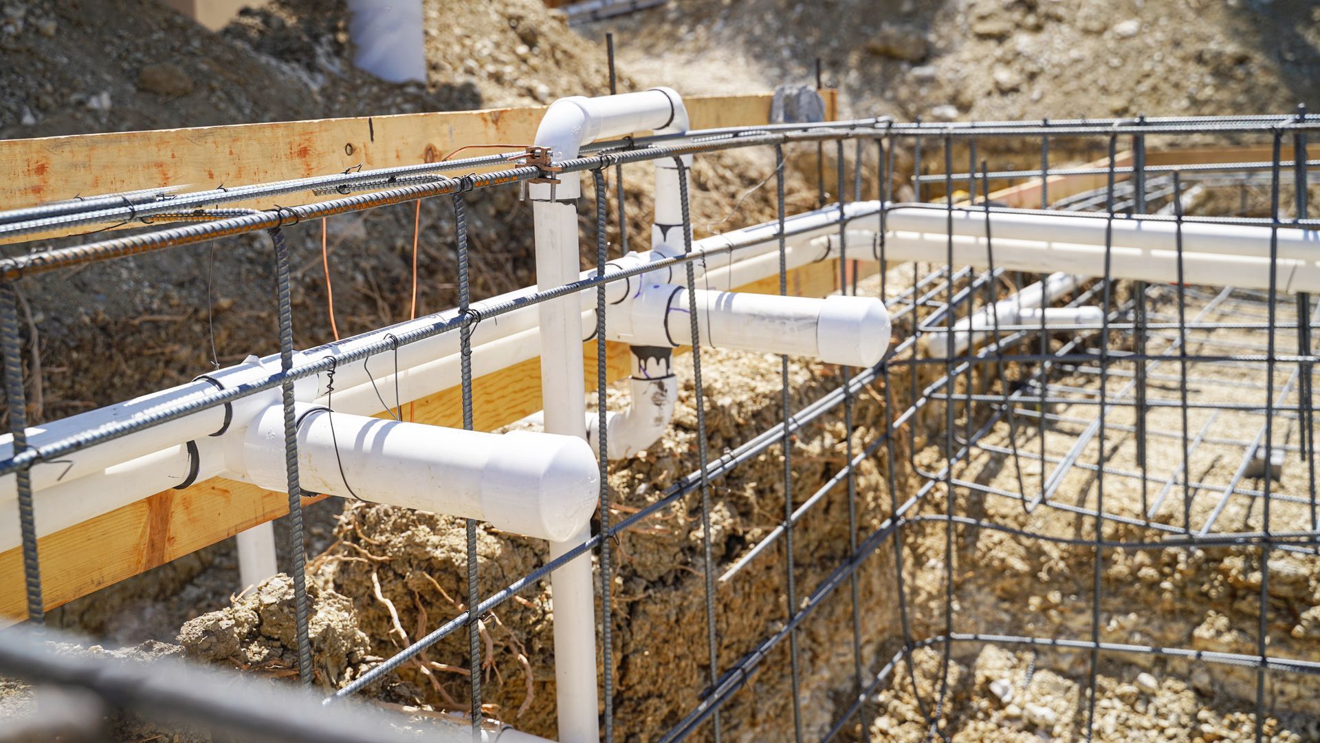 Des tuyaux et des barres d'armature sont disposés au-dessus de fondations creusées lors de la construction d'une piscine.
