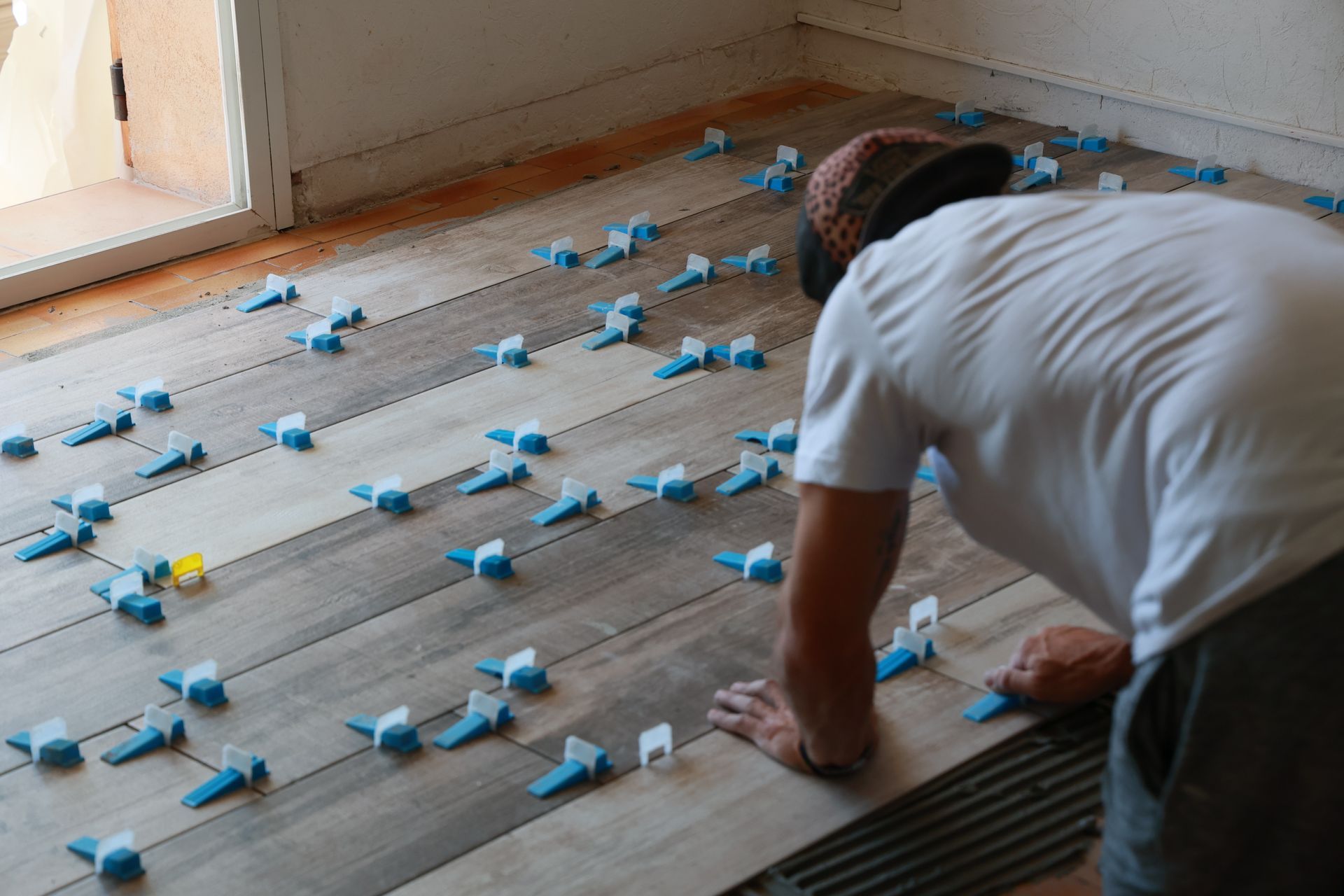 Ouvrier installant des croisillons bleus sur un carrelage lors d'une rénovation.