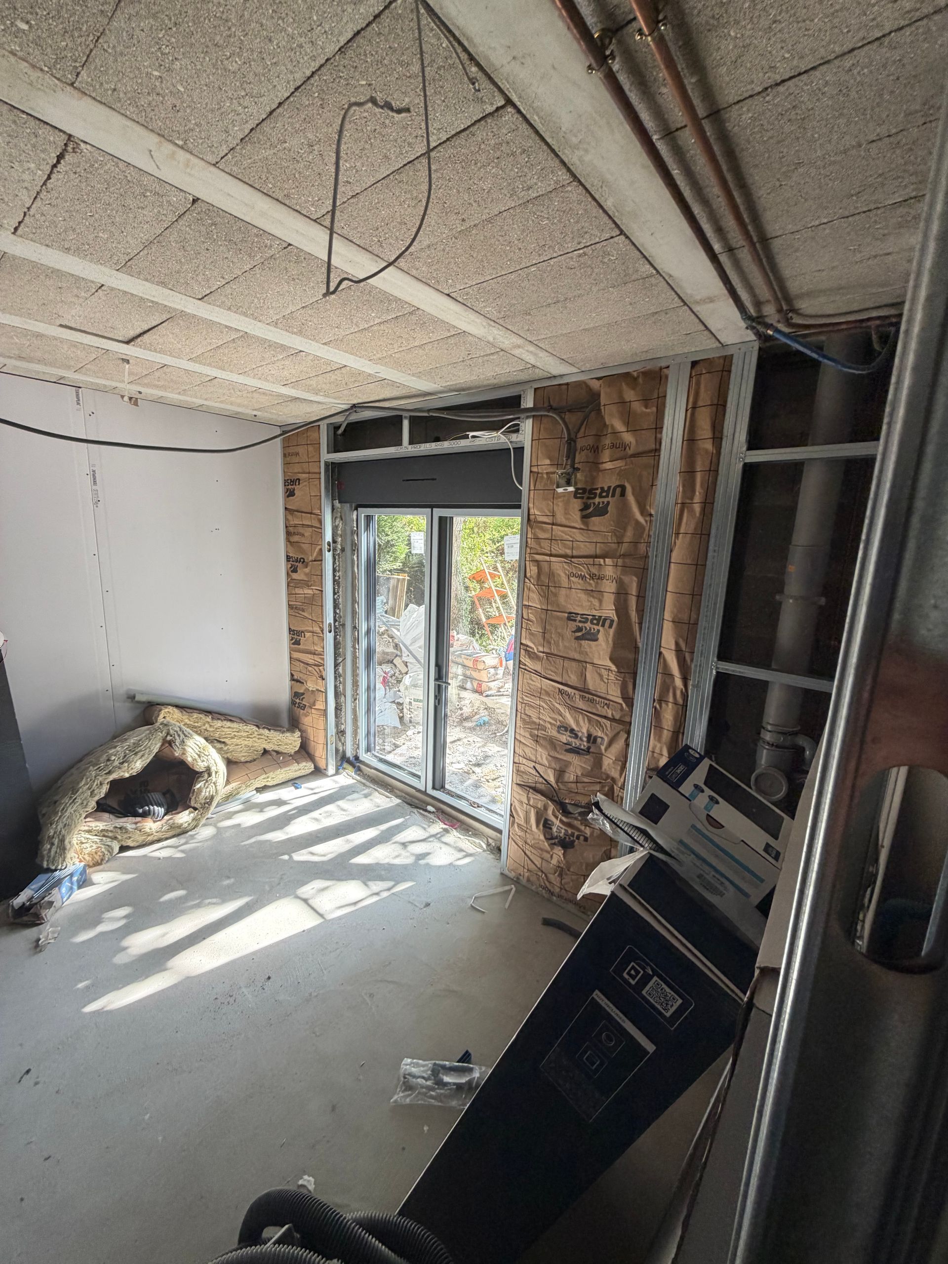 Une extension de maison inachevée avec un plafond apparent, un mur de briques et matériaux de construction au sol.