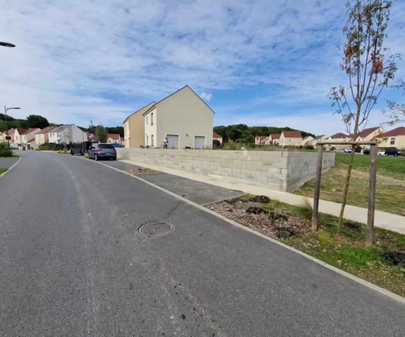 Rue résidentielle tranquille bordée de maisons, avec une voiture garée et un muret en pierre.