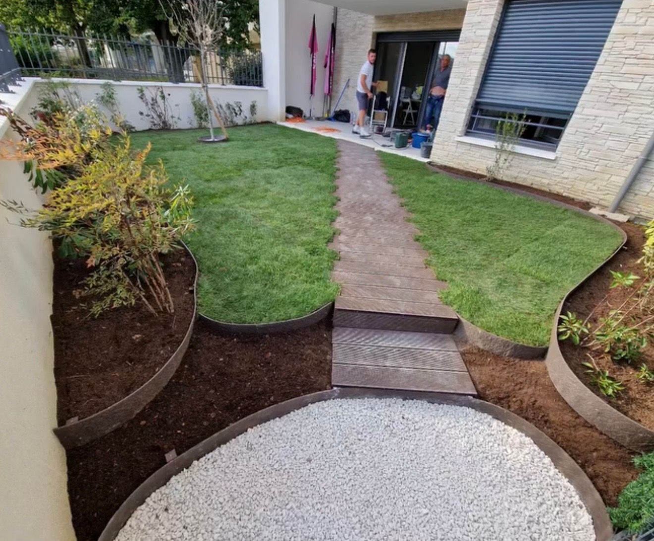 Allée de jardin avec dalles de pierre, bordures courbes, pelouse verte et cercle de gravier.