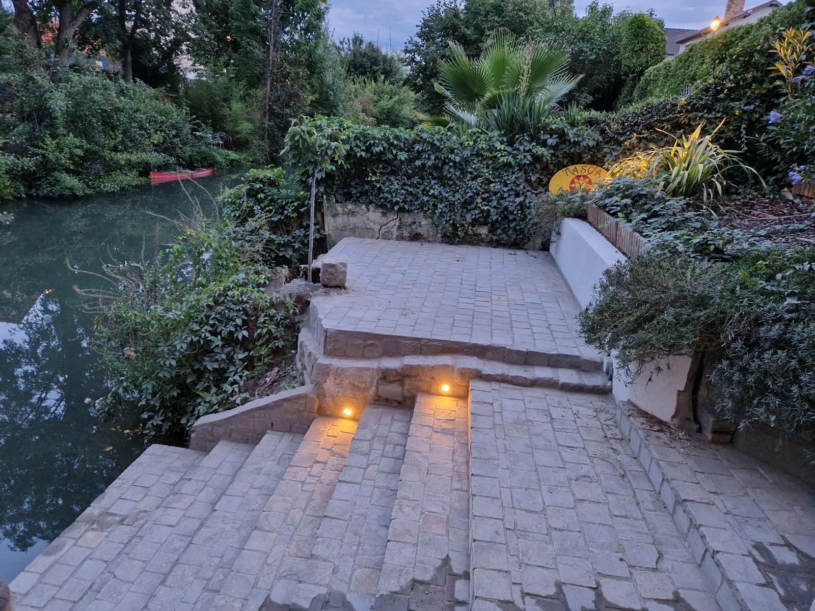 Terrasse en briques dans un jardin luxuriant au bord de la rivière, vue le soir.