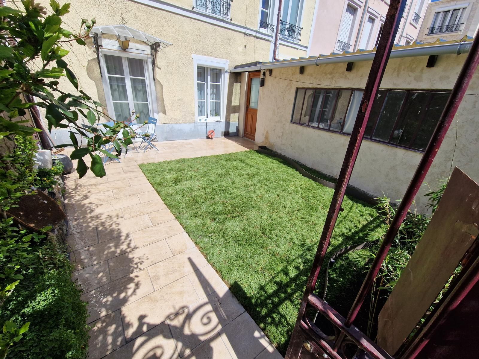 Petite cour avec pelouse, chemin de pierres et murs beige baignés de soleil.