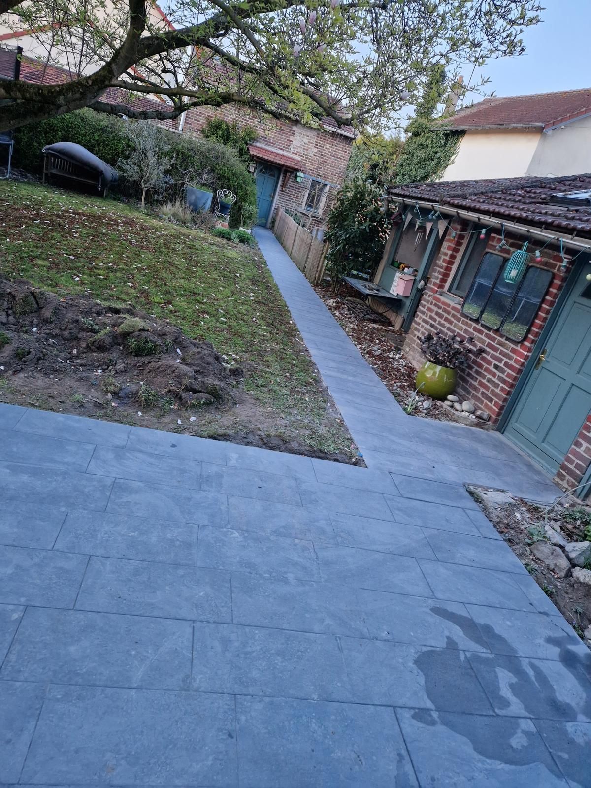 Terrasse arrière avec allée en dalles, muret en briques et petit jardin bordé d'arbres.