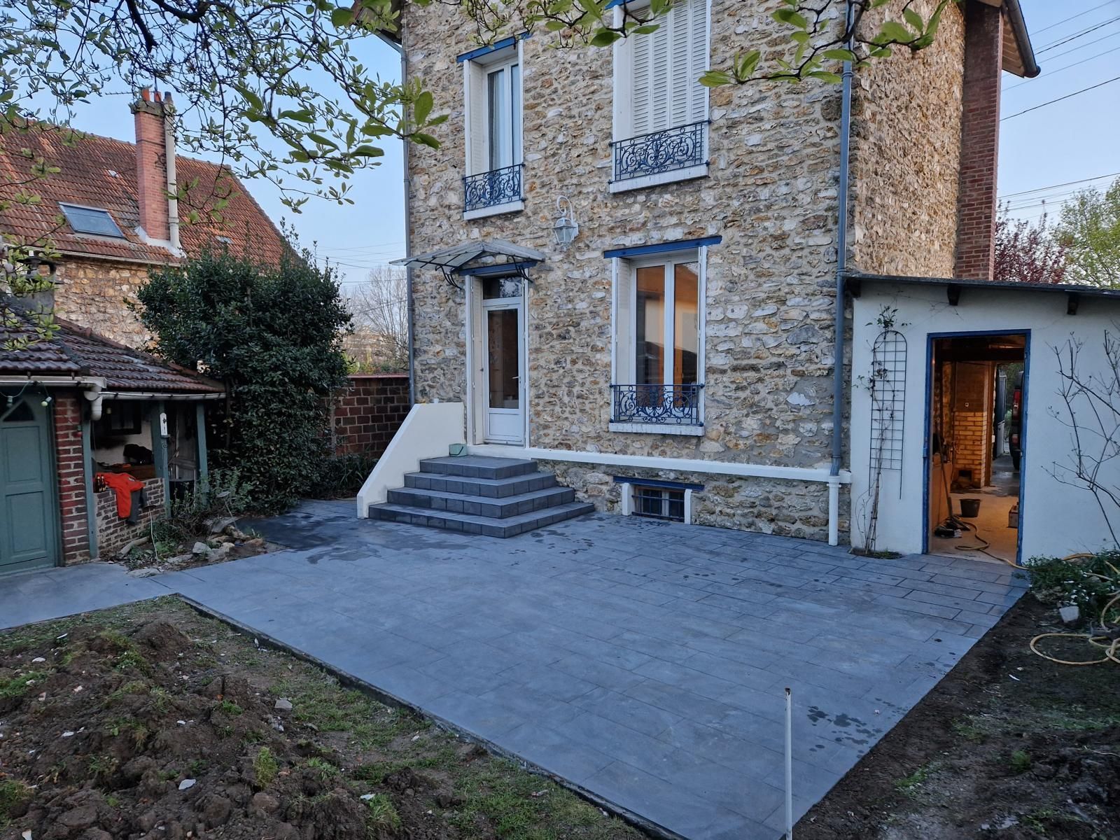 Cour d'une maison en pierres avec terrasse en carrelage, marches menant à la porte et petite dépendance latérale.