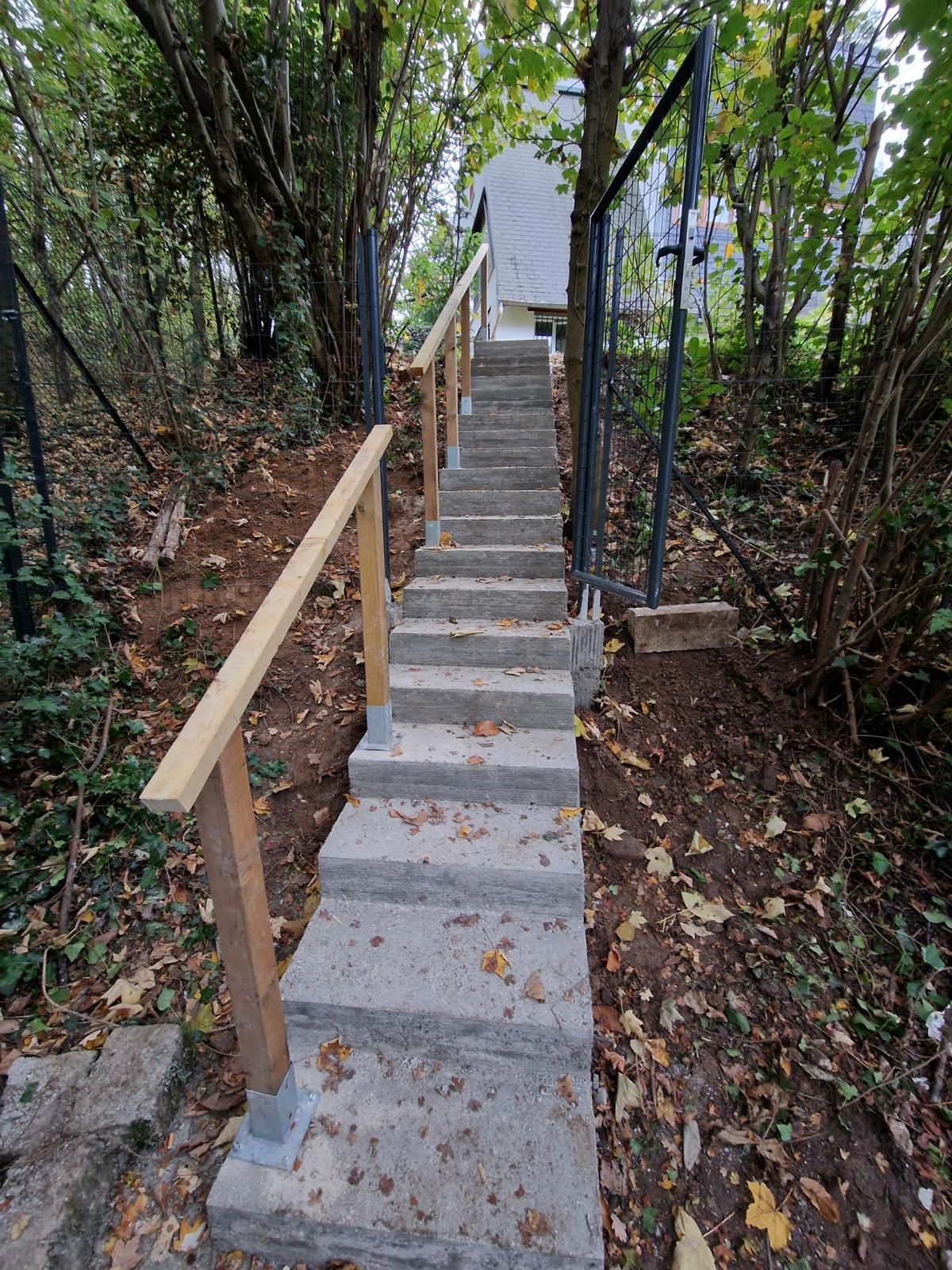 Escalier en béton avec rampes en bois menant à travers un flanc de colline boisé.