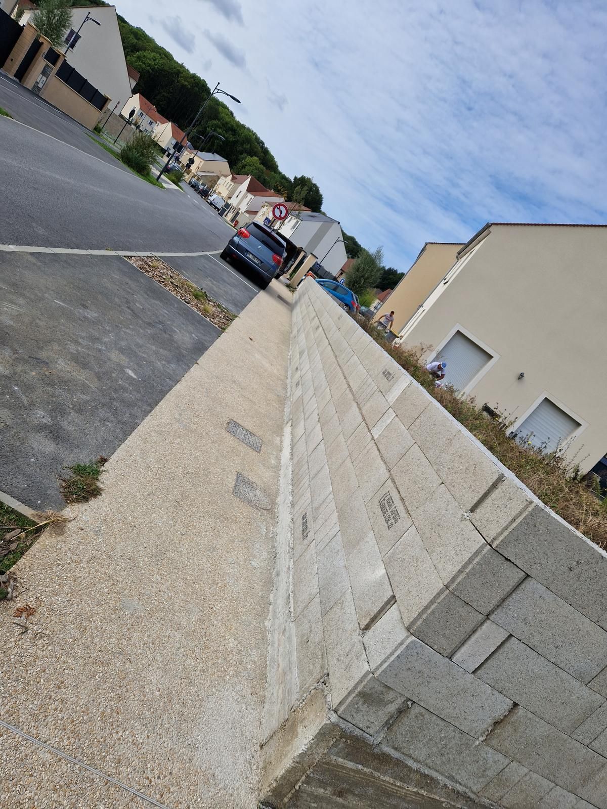 Rue résidentielle avec une voiture bleue garée à côté d'un mur beige.