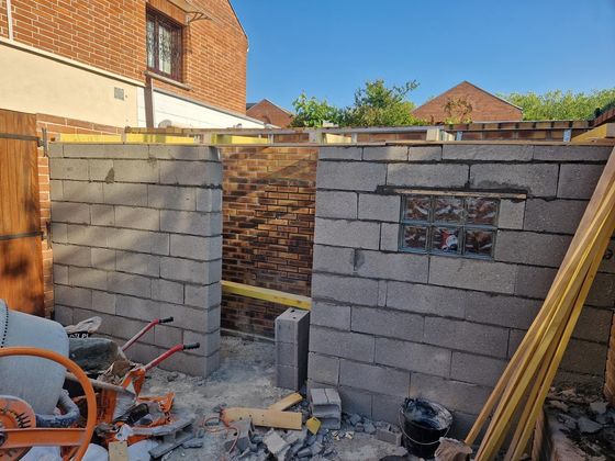 Mur de briques partiellement construit dans une cour arrière, avec des outils et des matériaux de construction.