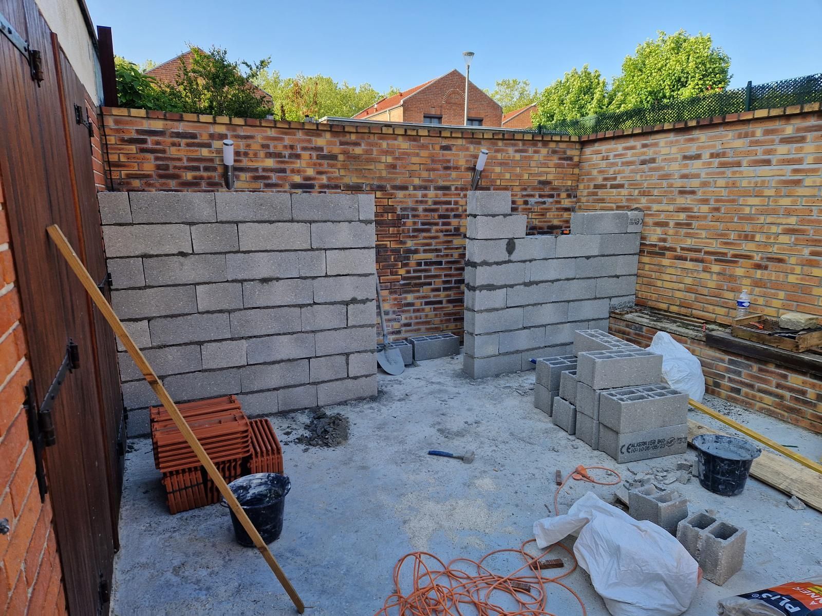 Une annexe de maison en cours de construction, avec des matériaux de construction et des outils éparpillés.