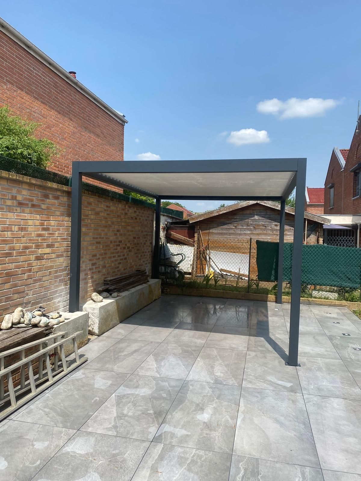 Cour carrelée vide avec une pergola en métal sombre.