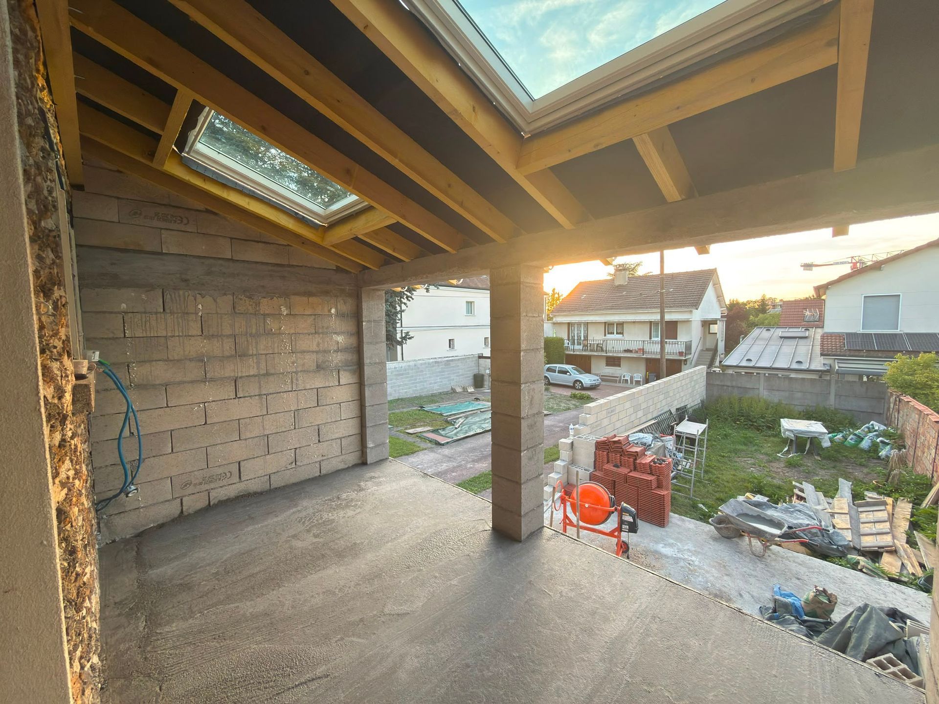 Extension en construction avec poutres apparentes et mur de briques.