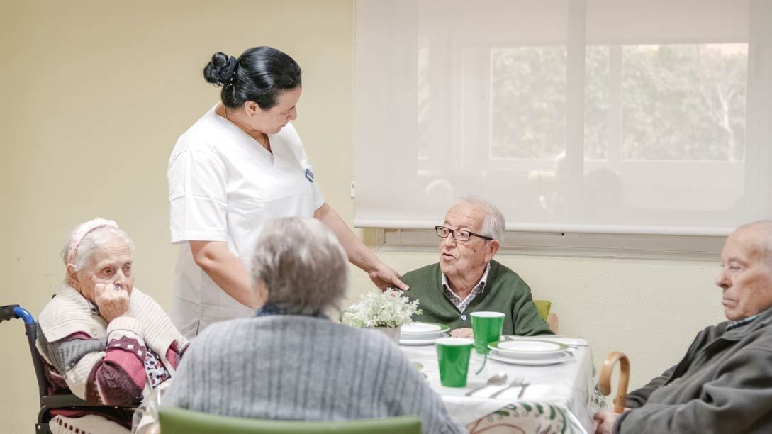 Una enfermera está hablando con un grupo de personas mayores sentadas en una mesa.