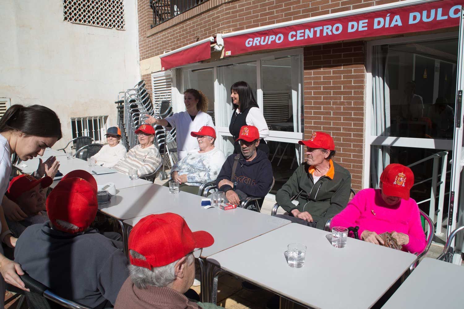 Un grupo de personas están sentadas en mesas afuera de un edificio que dice 