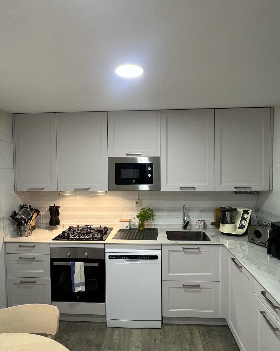 Una cocina con gabinetes blancos, una estufa, un microondas, un fregadero y una mesa.