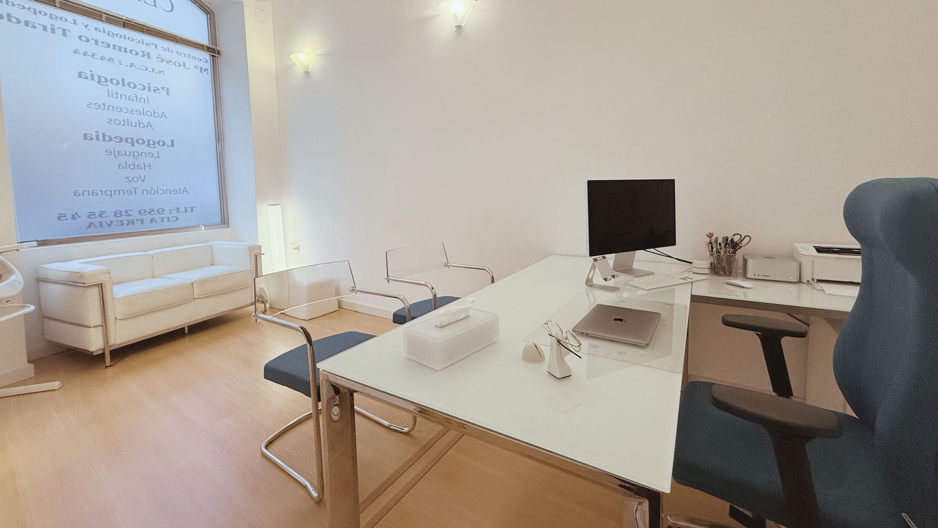 Un escritorio blanco con una computadora encima en una habitación con una silla azul.