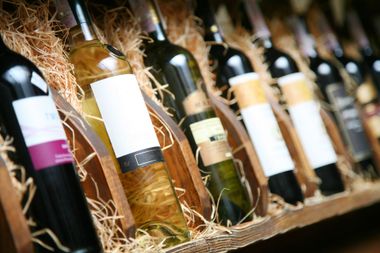 Des rangées de bouteilles de vin sur de la paille, disposées en biais sur des étagères en bois dans une cave ou une vitrine de magasin.