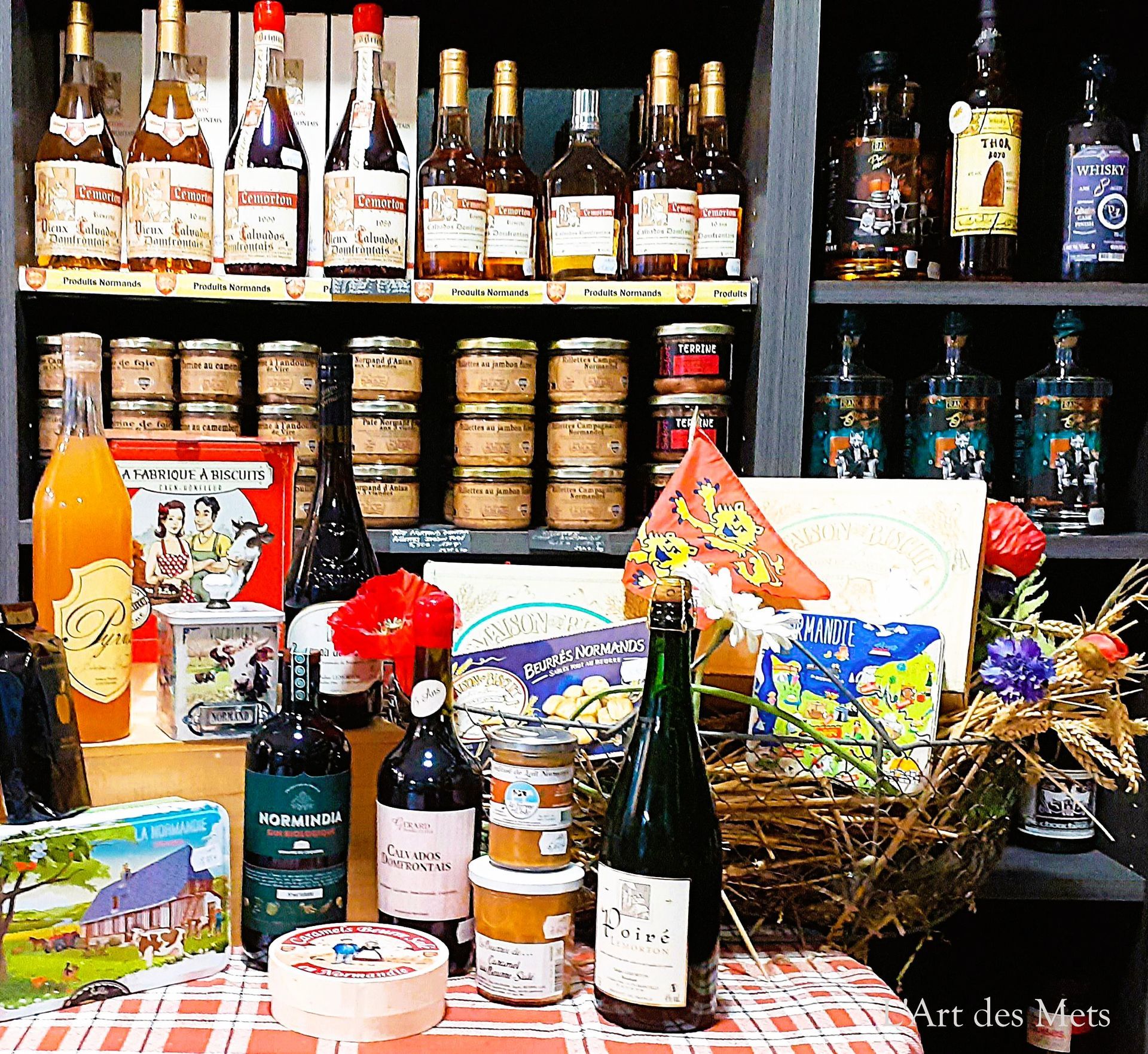 Des bouteilles, des bocaux et des paniers cadeaux assortis sont présentés sur des étagères, ainsi qu'une nappe à carreaux, dans un magasin.
