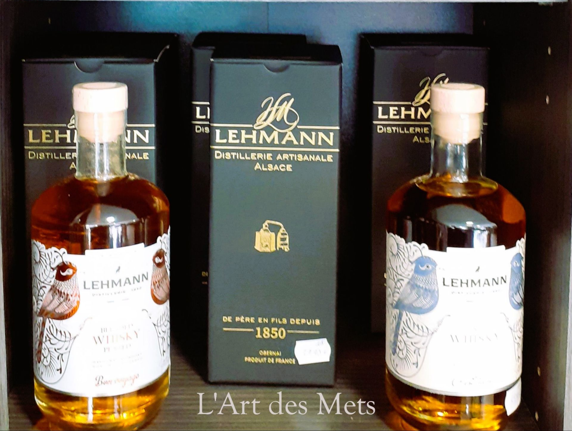 Deux bouteilles Lehmann encadrent une boîte Lehmann sur une étagère.