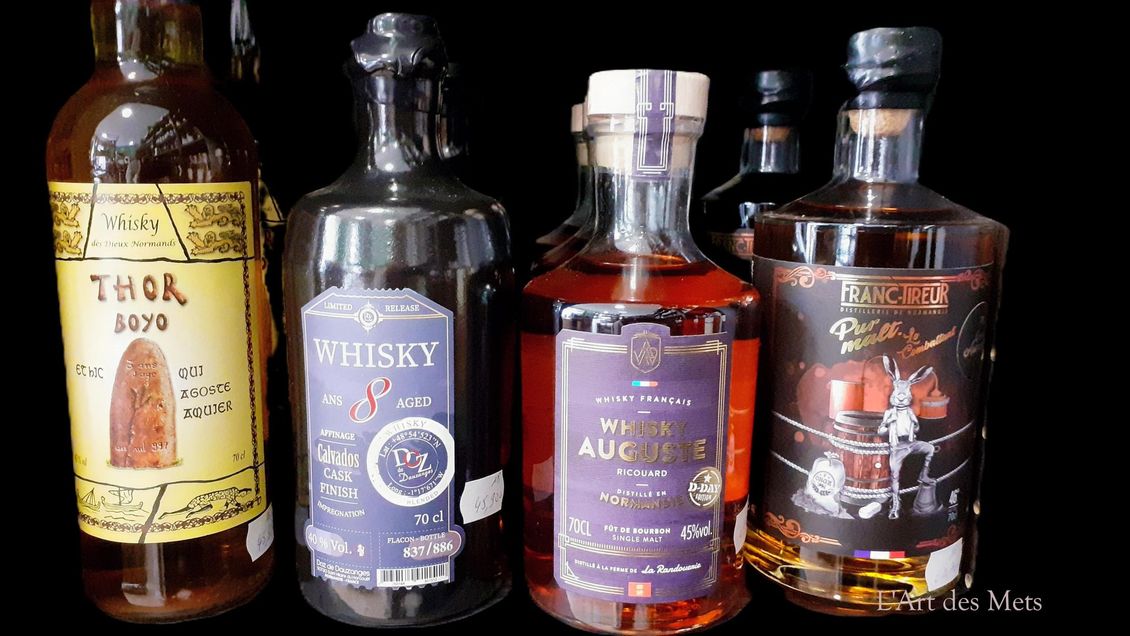 Quatre bouteilles de whisky sur une surface sombre, avec des étiquettes.