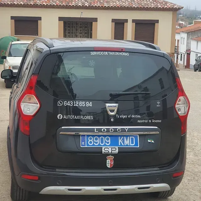 Taxi Dacia Lodgy gris oscuro con matrícula española. Tiene el número de teléfono y la información del servicio de taxi en la luneta trasera.
